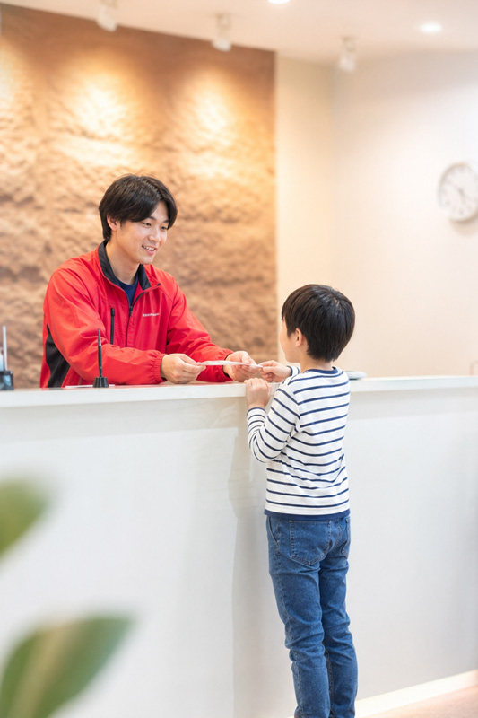 受付カウンターで会員証を差し出す子どもの画像