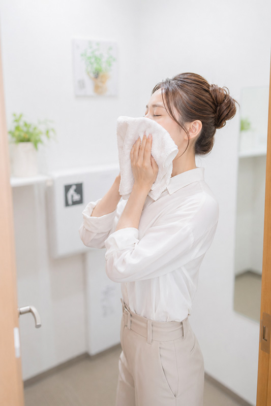 更衣室で髪を上げ、顔にタオルを押し当てるOLの画像